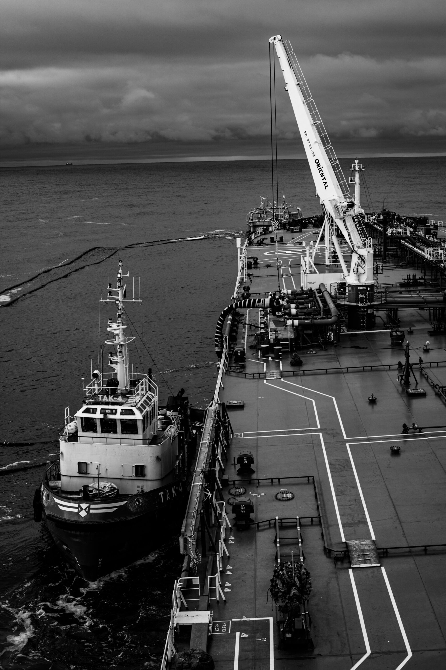 Aerial view of a cargo ship docked at an ocean terminal in monochrome tones.